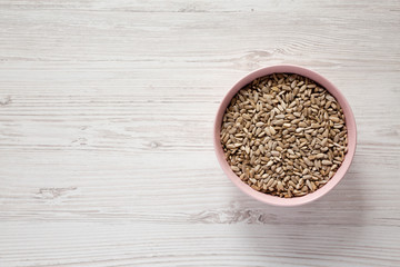 Hulled sunflower seeds in a pink bowl over white wooden surface, overhead view. Flat lay, overhead, from above. Copy space.