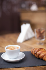 Close up of cup of coffee served with croissant in a cozy coffee shop