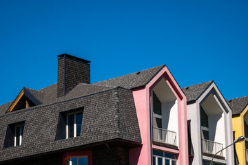 Rows of triangular elements of roofline covered with shingle, with chimney against blue sky