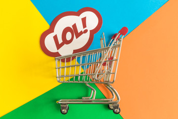 Flat lay of shopping cart and lol text in speech bubble against colorful background minimal creative concept.