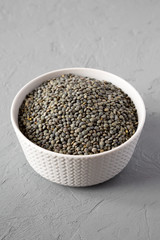 Dry green french lentils in gray bowl  over gray surface, side view. Close-up.