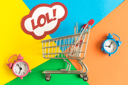 Flat lay of shopping cart and lol text in speech bubble with alarm clocks against colorful background minimal creative concept.