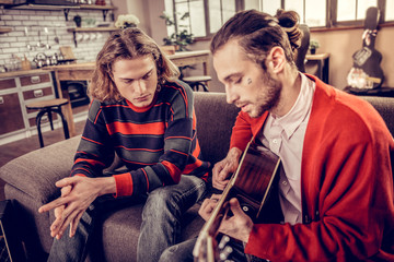 Bearded musician wearing white shirt and red cardigan playing guitar
