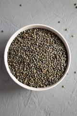 Dry green french lentils in a gray bowl over concrete background, overhead view. Top view, from above, flat lay.