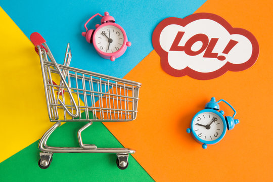 Miniature shopping trolley with alarm clocks and label with lol text on multicolored background abstract.
