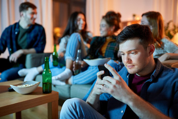 technology, internet addiction and people concept - man with smartphone at home friends party in evening