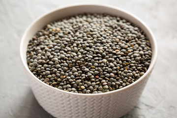 Dry green french lentils in a gray bowl over concrete surface, side view. Close-up.