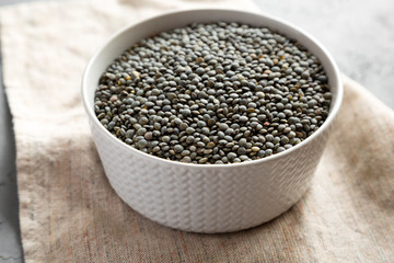 Dry green french lentils in a gray bowl, side view. Close-up.