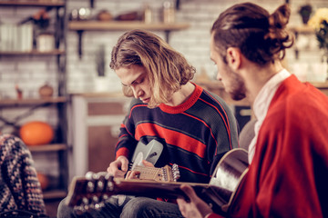 Young man wearing striped sweater learning to play guitar