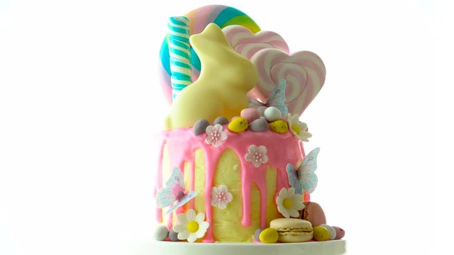 On-trend Easter theme candy land drip cake decorated with lollipops, cand eggs and white chocolate bunny on white background.