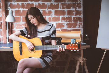 Young beautiful Asian woman is playing acoustic guitar at her working room, vintage warm tone