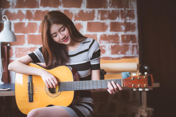 Young beautiful Asian woman is playing acoustic guitar at her working room, vintage warm tone