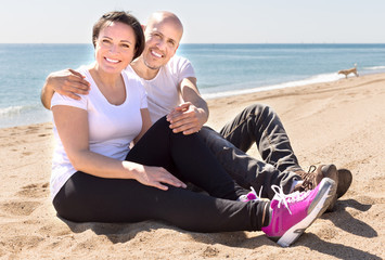 couple of elderly man with a woman in white shirts sitting on sand on beach