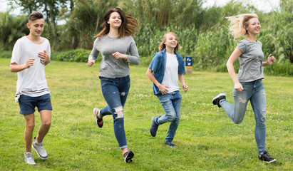 Obraz na płótnie Canvas teenagers running through green lawn in summer in park