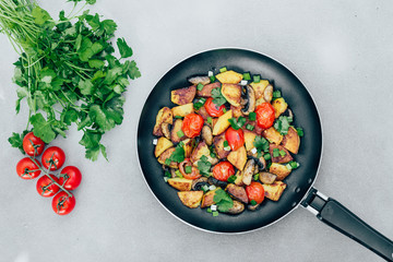 Fried potatoes in a pan with tomatoes, mushrooms, parsley on the table vegetarian food Top View - Image