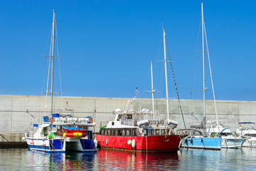 Fishing boats and private yachts moored at pier in seaport Blanes. Vessels with catch of sea fish delicacies. Sailing and motor boats are moored at concrete seawall. Marina Blanes, Spain, Costa Brava