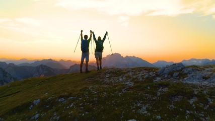 AERIAL: Young hiker couple outstretch their arms as they catch the sunset.