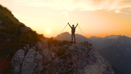 LENS FLARE: Excited man outstretches arms as he sees the sunset from a cliff.