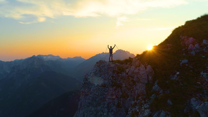 DRONE: Golden morning sun rays shine on excited trekker standing on a cliff.