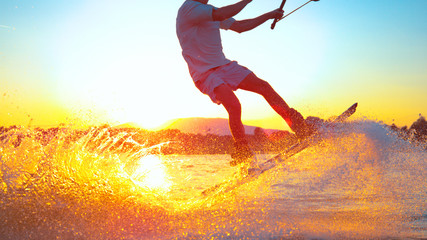 SUN FLARE: Cool surfer dude does 180 ollie while wakeboarding on sunny evening - obrazy, fototapety, plakaty