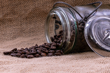 Antique jar with coffee beans spilled out onto a burlap sack