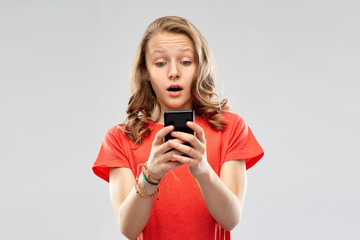 technology, emotions and people concept - terrified teenage girl in red t-shirt using smartphone over grey background