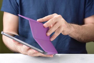 Blurred caucasian man using a digital tablet. White man puts on a new purple leather case on tablet with selective focus. male hands are holding a new tablet and putting on a violet cover. 
