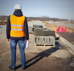 Fototapeta premium An engineer in a signal vest and protective helmet checks the quality of construction of a new road, industrial