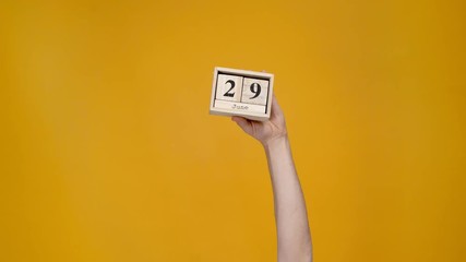 cropped view of woman presenting wooden calendar with 29 june date isolated on yellow