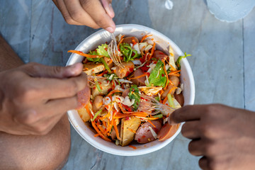 Three male hands with forks eat thai vegetable salad along with sausages, top view, closeup