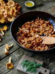 Fried chanterelle mushrooms with onion in frying pan on wooden background.
