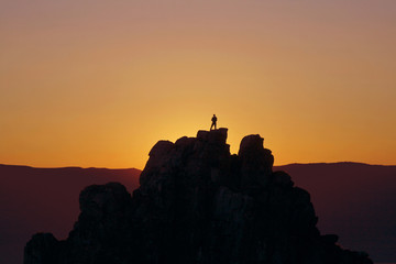 Naklejka premium silhouette of a man standing on top of a mountain against the sunset sky