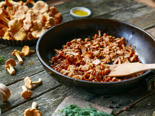 Fried chanterelle mushrooms with onion in frying pan on wooden background.