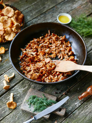 Fried chanterelle mushrooms with onion in frying pan on wooden background.