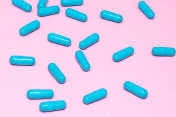 Bright blue pills on pink background close up