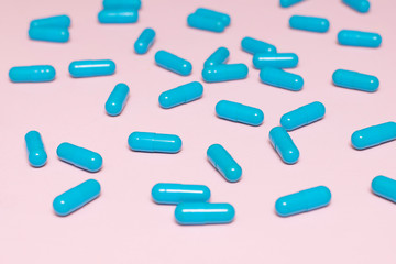 Blue pill capsules on pink background close up