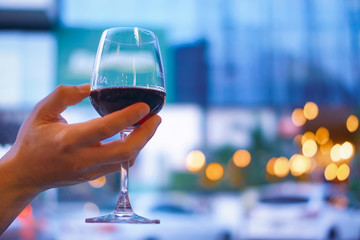 Hand held a glass of wine under evening light situation, this for relaxation after work or for celebrate in special day, bokeh background with city night lighting, With copy space