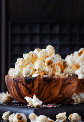 Salted popcorn in a wooden bowl, unhealthy food, dark wooden kitchen table background, selective focus