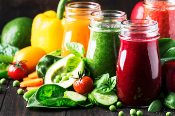 Multicolored vegan vegetable juices and smoothies from tomato, carrot, pepper, cabbage, spinach, beetroot in glass bottles on rustic kitchen table, vegetarian food and drink concept, selective focus