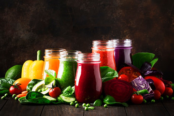 Multicolored vegan vegetable juices and smoothies from tomato, carrot, pepper, cabbage, spinach, beetroot in glass bottles on rustic kitchen table, vegetarian food and drink concept, selective focus