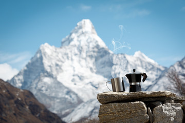Mug and coffee maker stand on the stones. The mountain is blurred. Steam from the mug. Ama Dablam....