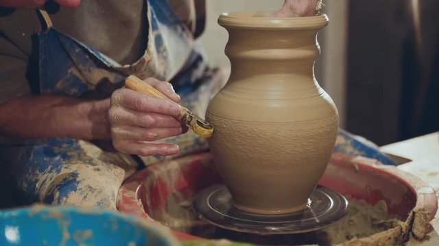 The potter making pattern on clay vase, using tool for it