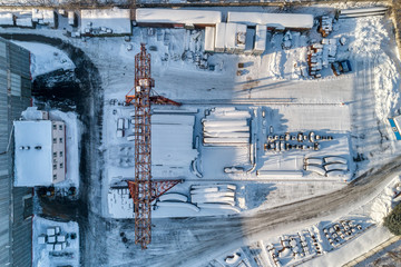 Open warehouse for storage of large diameter metal pipes. A gantry crane is installed in the territory. Winter sunny day.