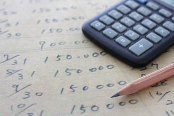 茶色い紙の上に書いた数字と計算機と鉛筆
