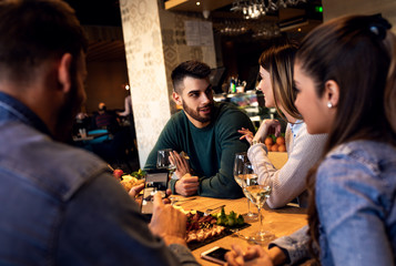 Group of young friends having fun in restaurant, talking and laughing while dining at table.