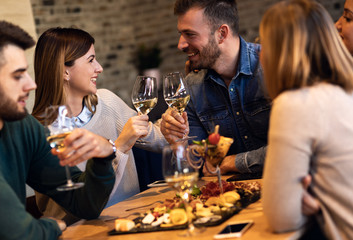 Group of young friends having fun in restaurant, talking and laughing while toasting with glass of...