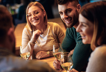 Group of young friends having fun in restaurant, talking and laughing while dining at table.