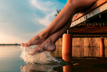Woman legs as she sitting on wooden dock by the lake.