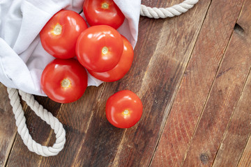 Close-up red tomatoes in eco-friendly reusable white linen bag on wooden table. 