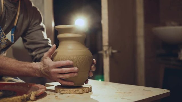 Potter's hands put handmade clay jug at camera